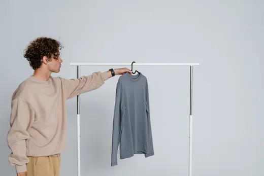 Hombre con sudadera beige y pantalón camel elige una camiseta gris de manga larga colgada en una barra