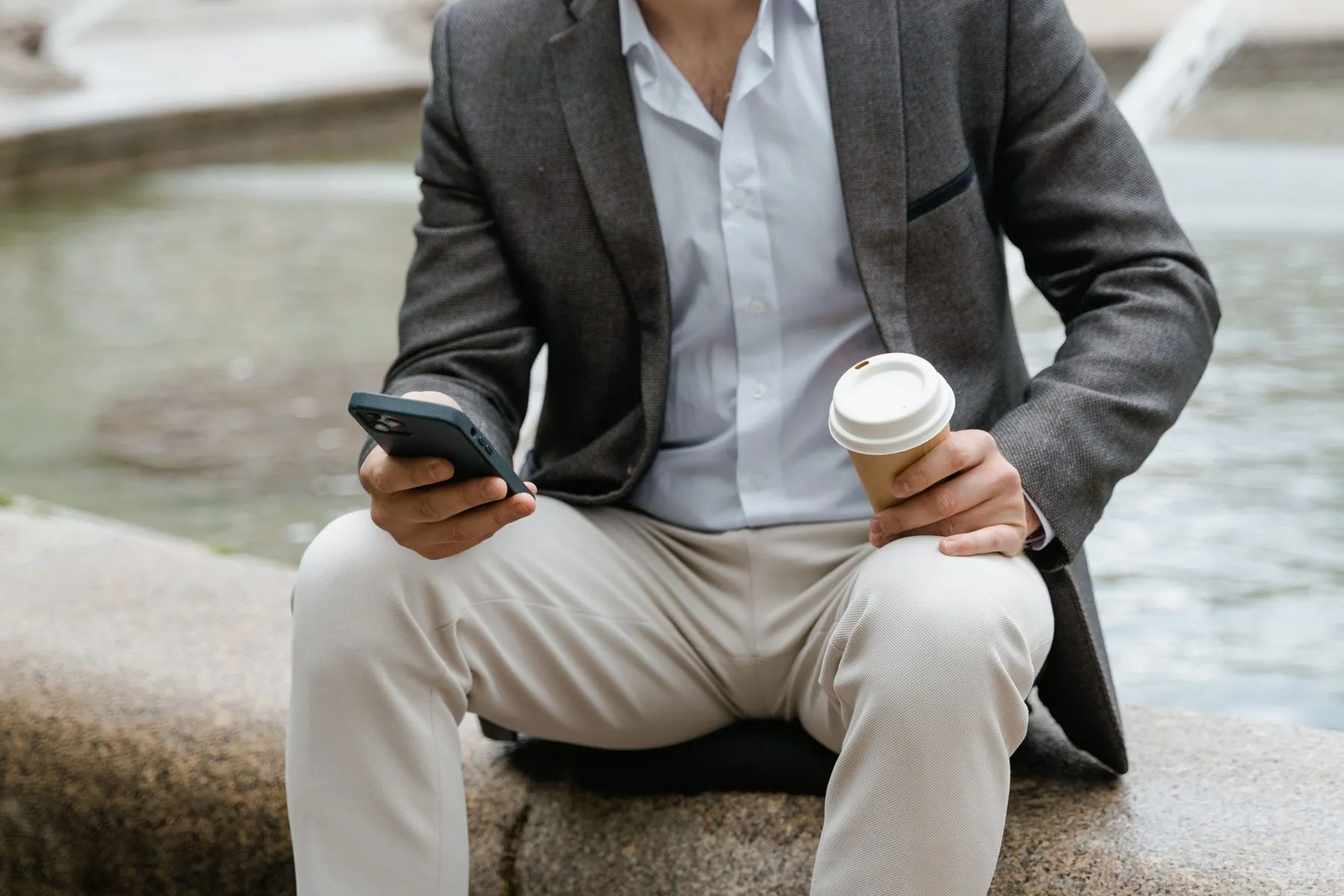 Hombre sentado con americana gris, camisa azul claro abierta y pantalón beige