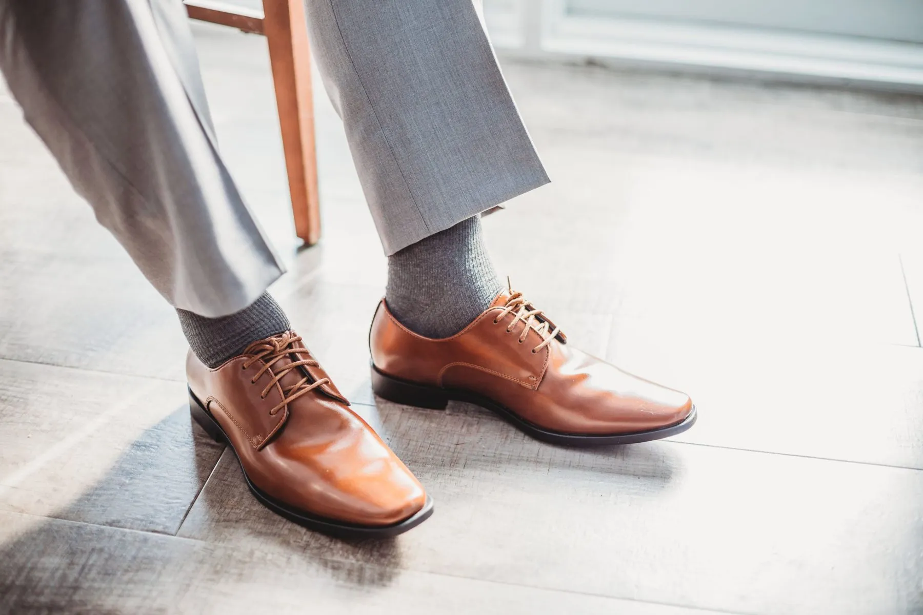 Pies de un hombre con pantalón gris, calcetines grises y zapatos derby de piel marrón con cordones